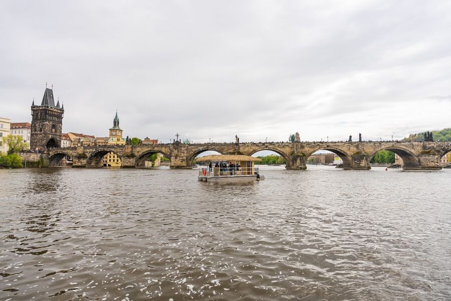 Prague: Party Tiki Boat Sightseeing Cruise with Drinks - A Tiki boat with Prague landmarks outside the rail